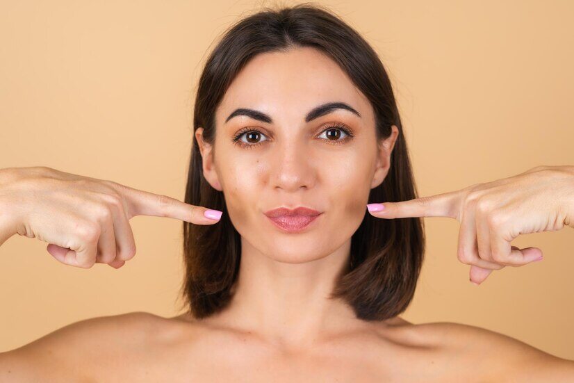 portrait-young-woman-beige-with-natural-makeup-with-bare-shoulders-points-her-fingers-lips_343596-7486